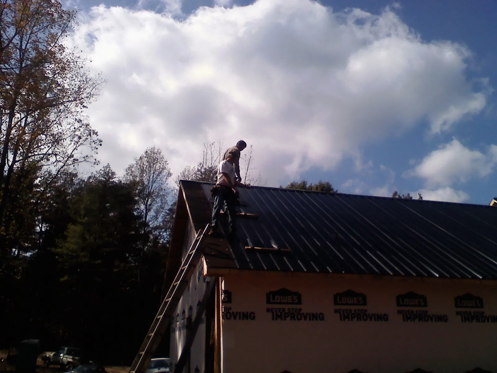 Roofer fastening dark metal panels high against a cloudy sky, from a Roof Inspection job in Milford